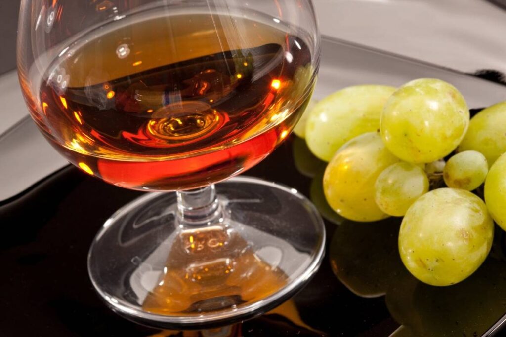 a glass of cognac with a bunch of grapes