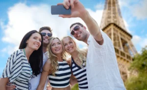 Group of friends smiling while taking a selfie in front of the Eiffel Tower in Paris on a bright summer day.