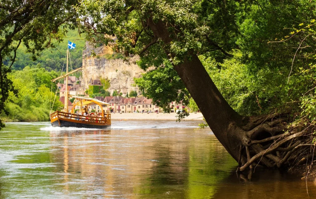 Traditional wooden gabarre boat cruising past La Roque Gageac on the Dordogne River