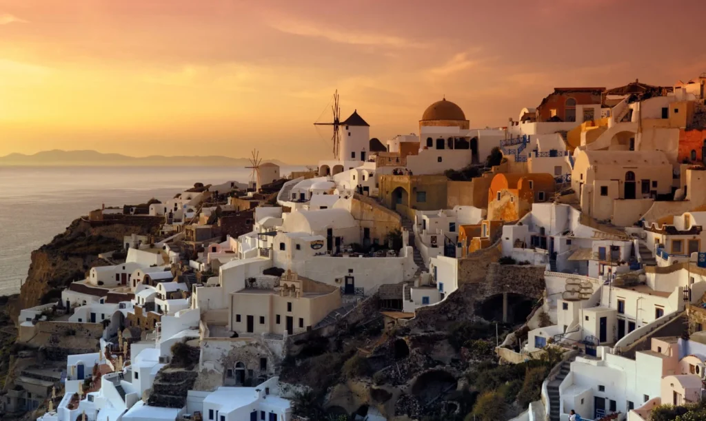 luxury holidays in europe: Whitewashed buildings and windmills of Oia in Santorini overlooking the Aegean Sea at sunset.