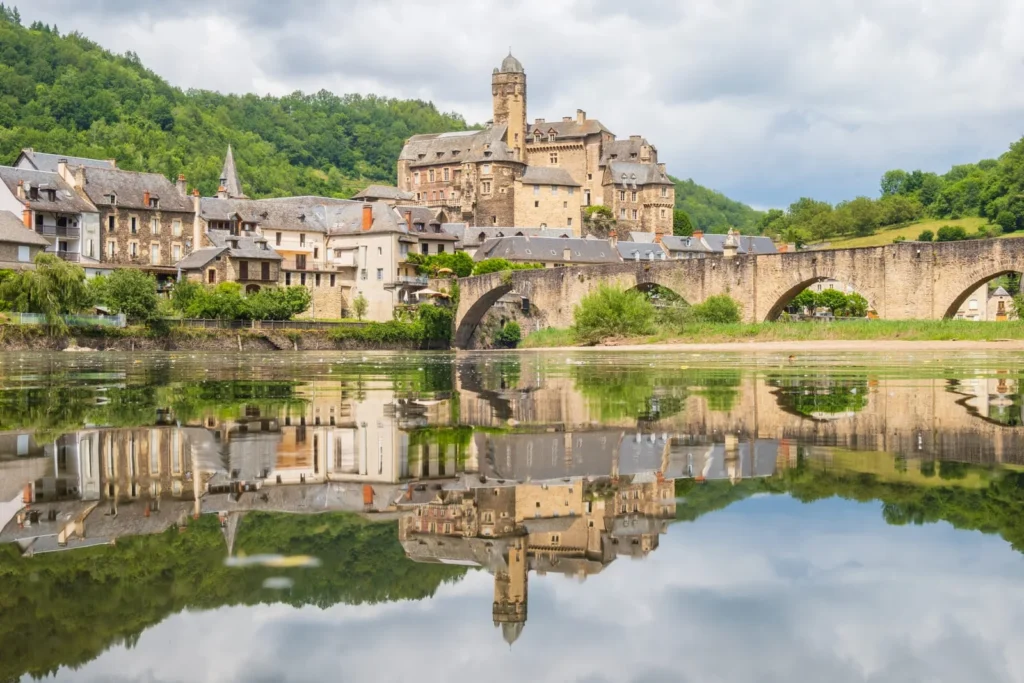 View of Estaing village with castle and stone bridge over the Lot River, reflecting medieval settlement patterns in France