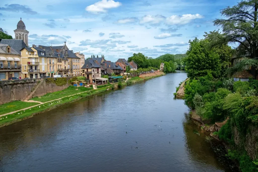 Small village on the Dordogne River with a hilltop castle and calm water