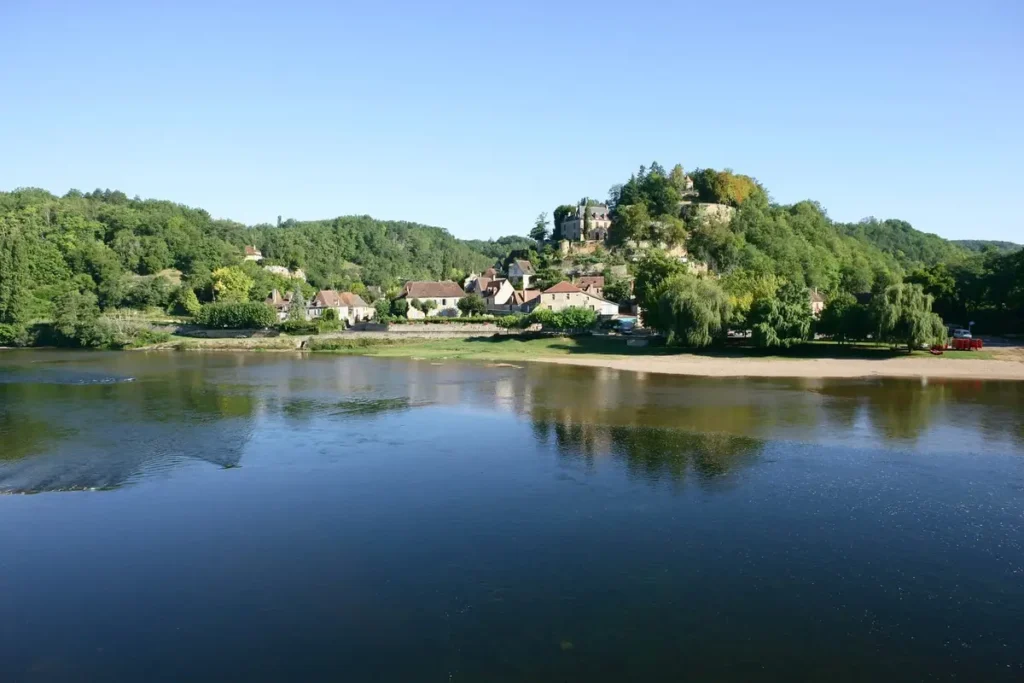 Historic riverside town along the Dordogne River with old buildings and trees