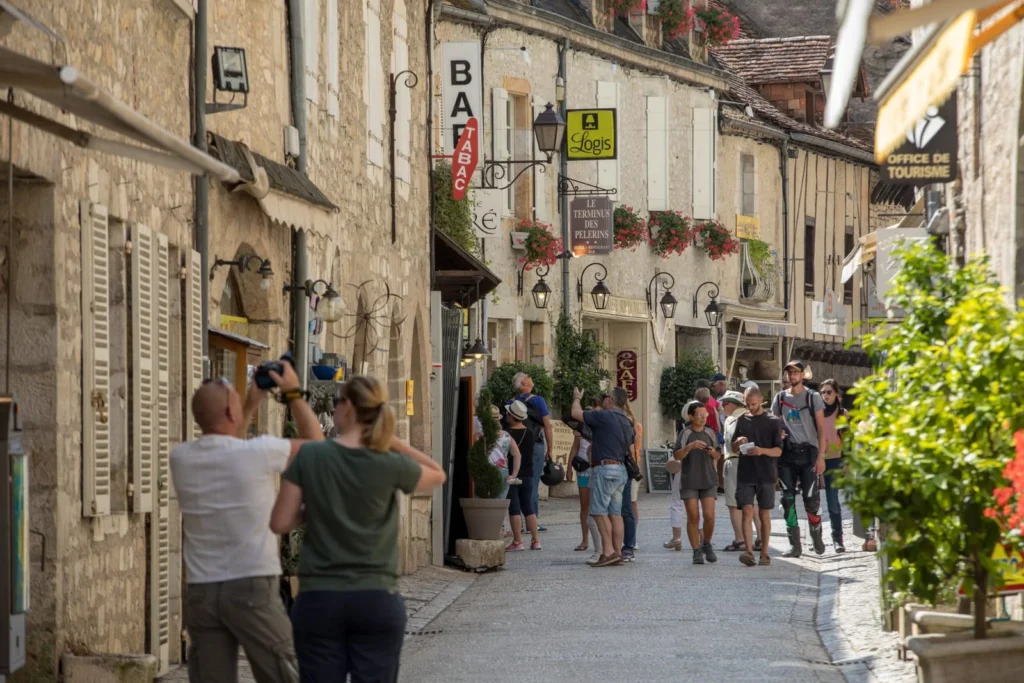 Tourists walking along a narrow medieval street lined with shops and cafés in Rocamadour
