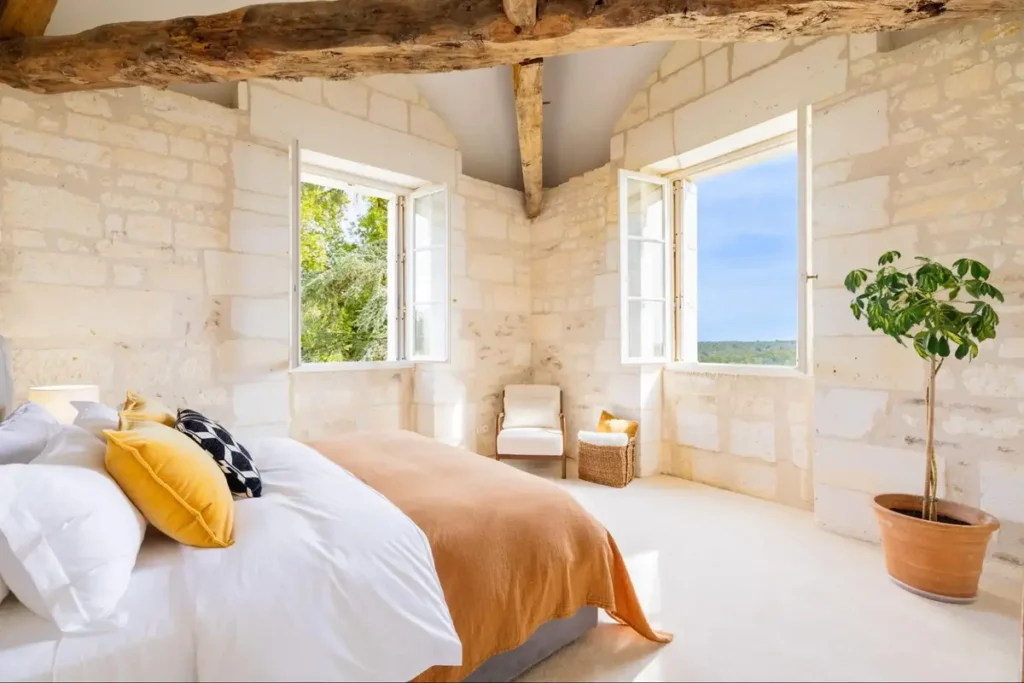 Bright château bedroom with stone walls, large windows, and rustic luxury design