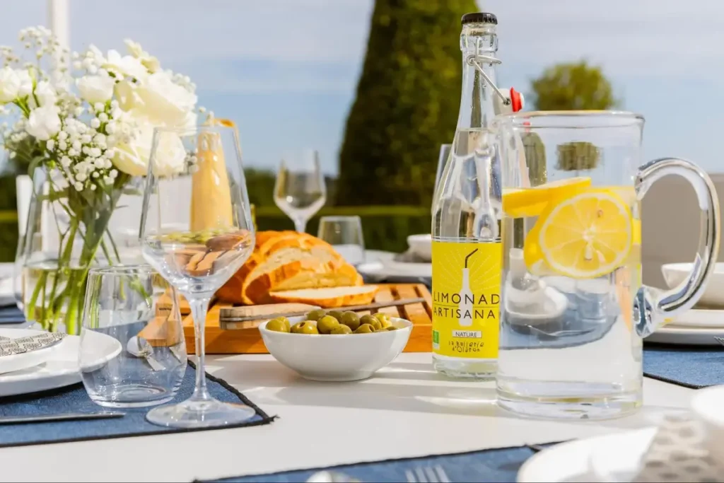 Outdoor dining table with lemonade, bread, olives, and glasses in sunny garden setting