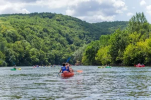 Kayakers paddling on the Dordogne River between green wooded banks