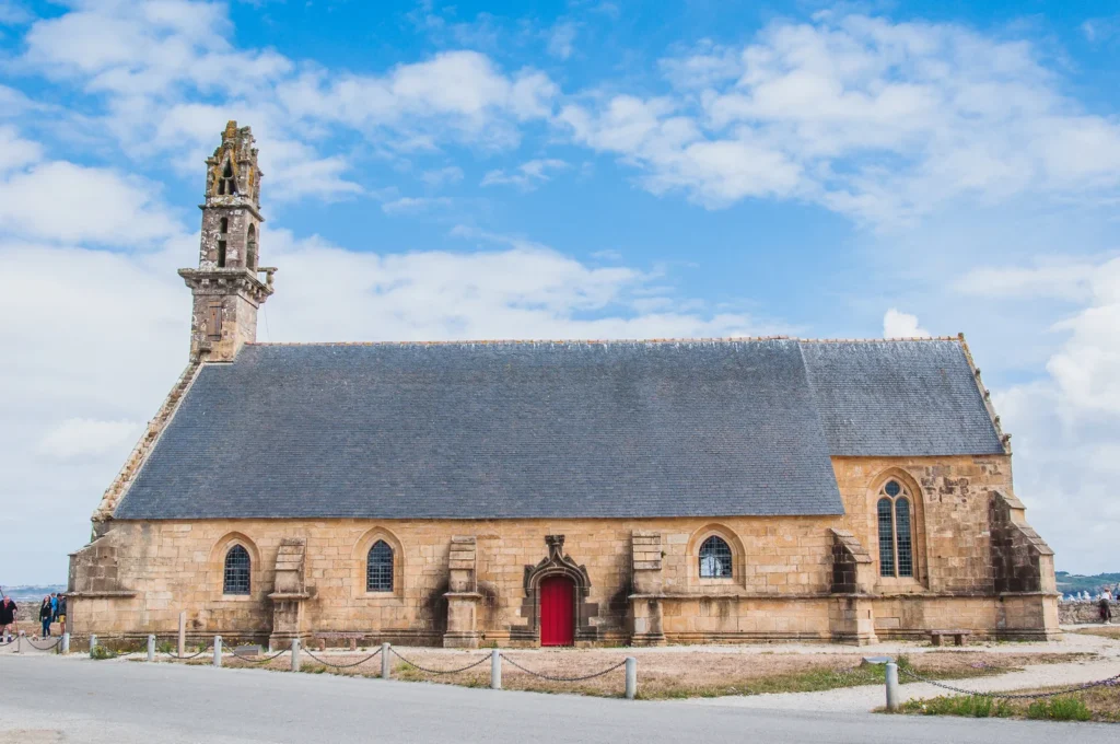 Old stone church with red door and bell tower under a blue sky in southwestern France