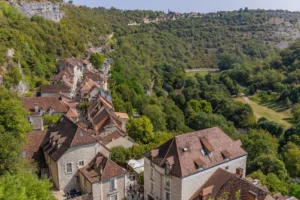 Elevated view of Rocamadour village with stone houses along the cliff and green Alzou valley below