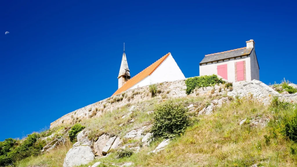 Small chapel and stone houses on a rocky hill under a clear blue sky in the French countryside