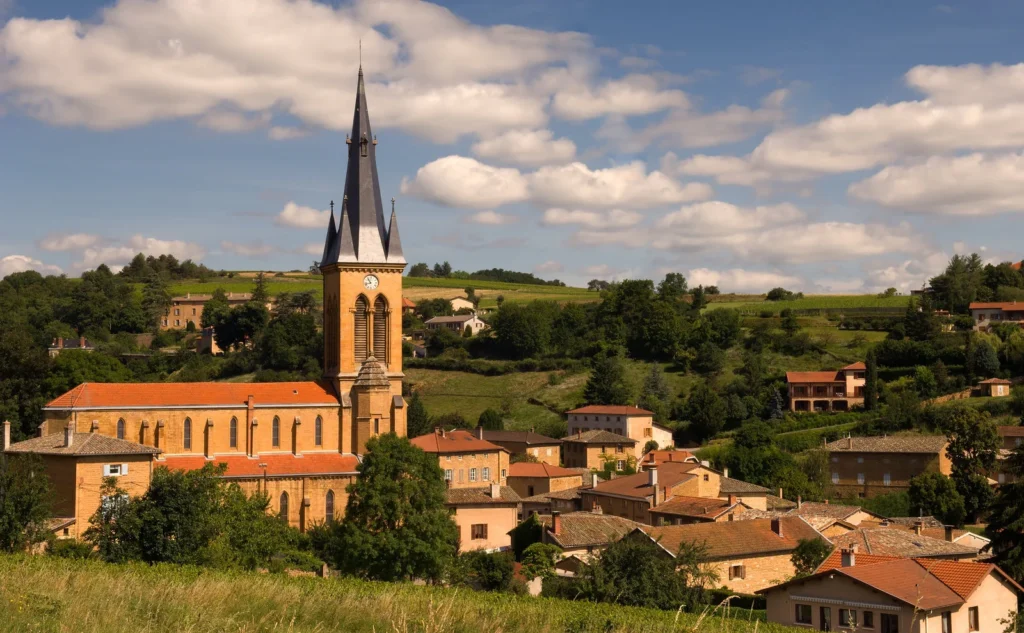 Small French village with church tower surrounded by rolling hills and vineyards under a clear sky