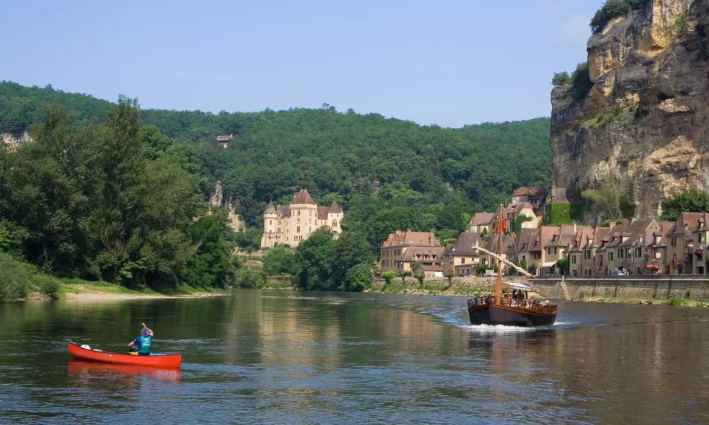Canoe and traditional boat on Dordogne River with cliffside village and castle views