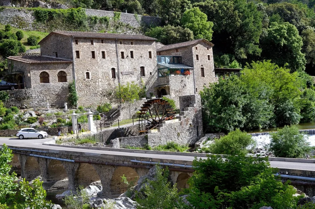 Historic stone watermill beside a river with a small bridge and lush greenery in the French countryside