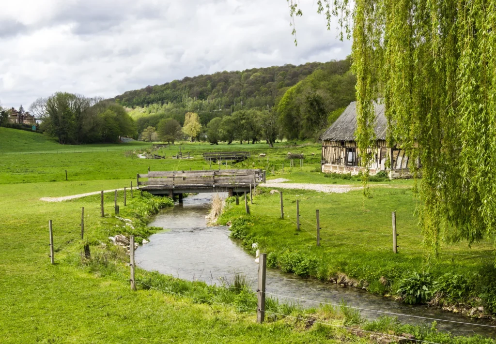 Peaceful French countryside with stream, wooden bridge, and green fields