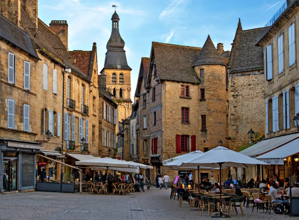 French town square with outdoor cafes, historic buildings, and evening atmosphere