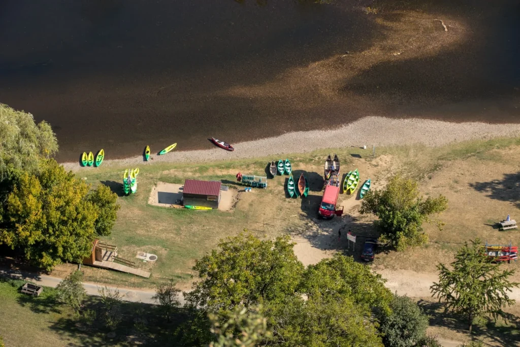 Canoe rental base on Dordogne River with kayaks lined along riverbank and launch area for canoe Dordogne trips