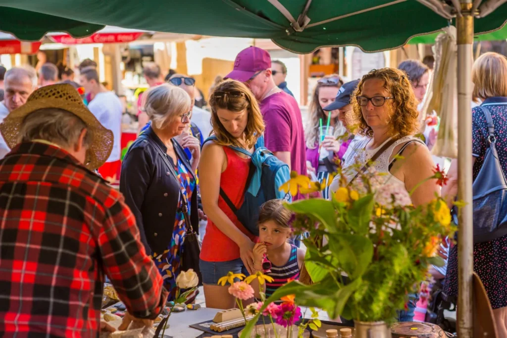 Busy outdoor market in Dordogne with locals and tourists browsing fresh produce and crafts