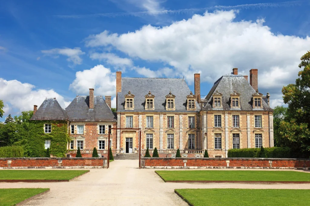 Historic French mansion with slate roofs, tall windows, brick walls, formal lawns, and a gravel entrance courtyard.