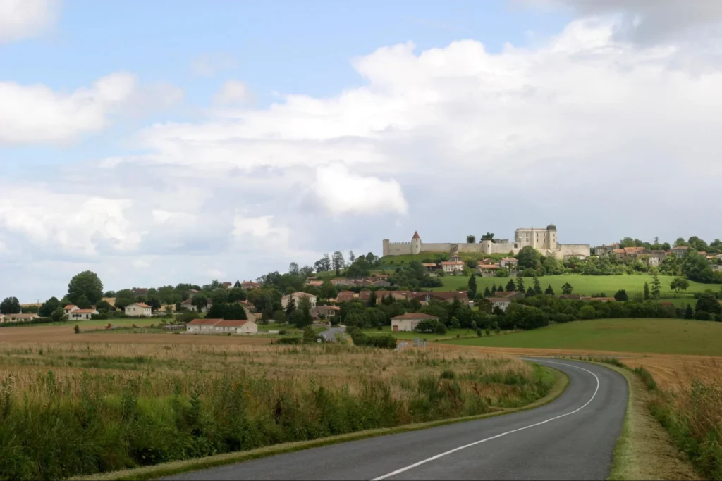 Scenic countryside road leading toward a hilltop village and château in rural France