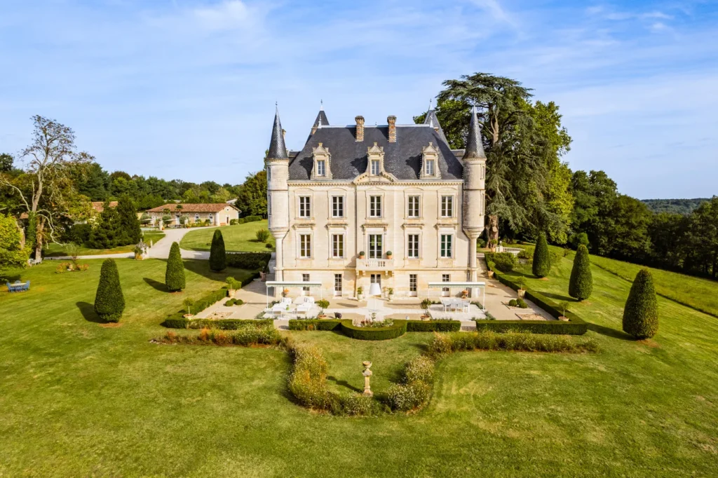 Château de Lasfonds framed by lawns, clipped topiary, terraces, and mature trees in rural France.