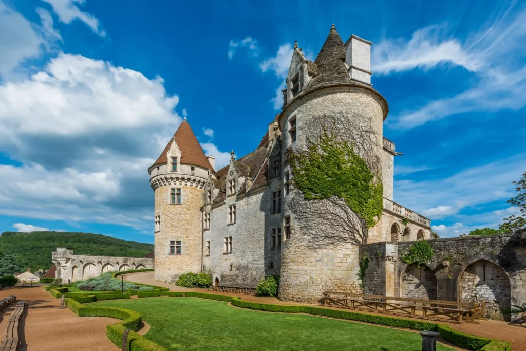 Historic Dordogne château with round stone towers, ivy covered walls, and manicured garden paths.
