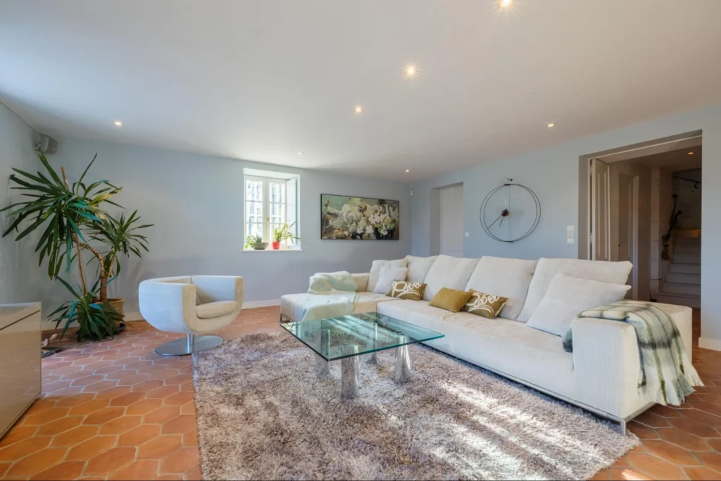 Elegant living room at Château de Lasfonds with a white sofa, glass coffee table, terracotta tile floor, and soft natural light