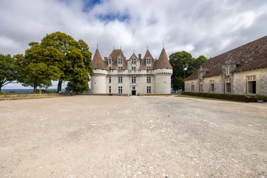 Wide exterior view of Château de Monbazillac with gravel courtyard and surrounding buildings in Dordogne, France