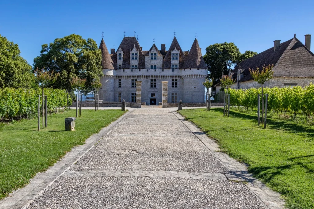 Front path leading to Château de Monbazillac with vineyard rows and stone towers in Dordogne, France