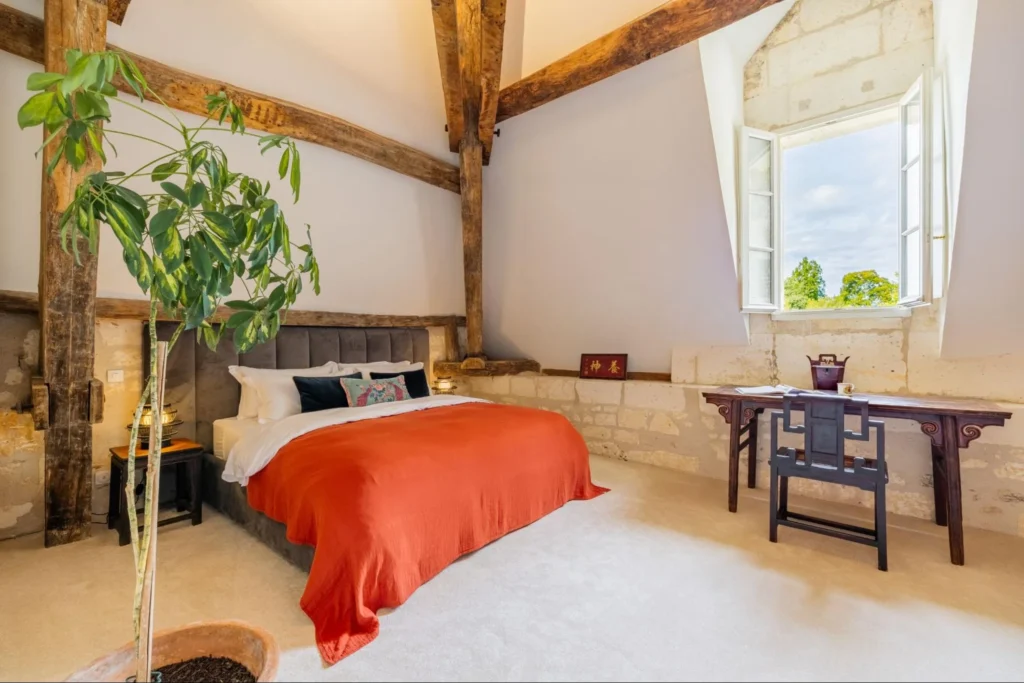 Cozy chateau bedroom with wooden beams, large bed, and countryside window view