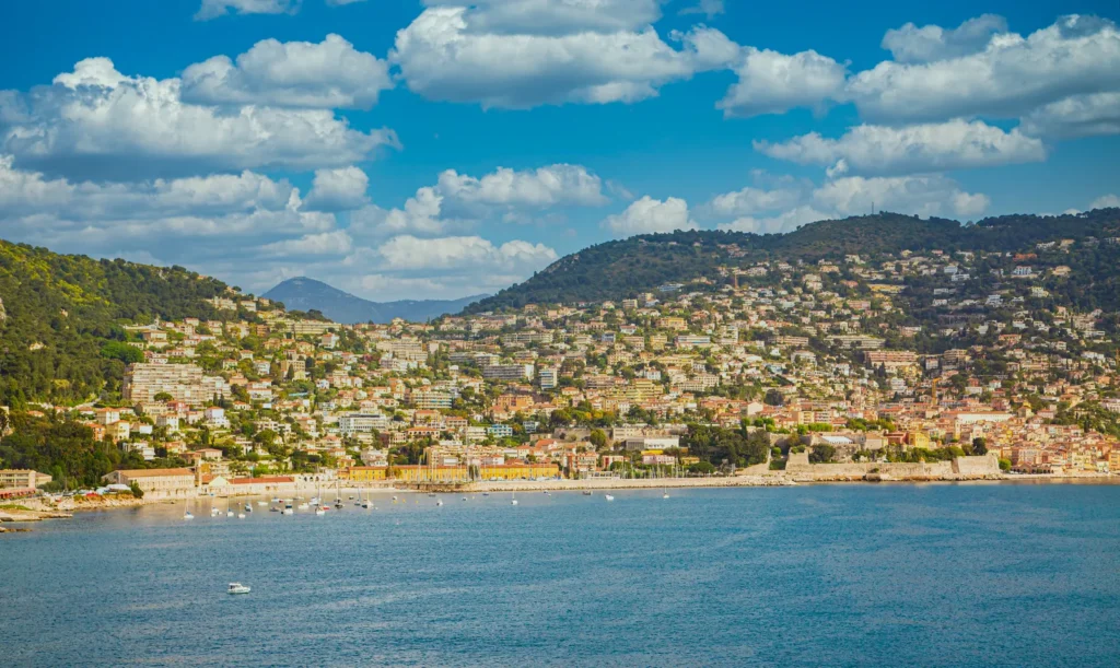 Panoramic view of a charming French Riviera coastal town with hillside homes, waterfront promenades, and a calm Mediterranean bay
