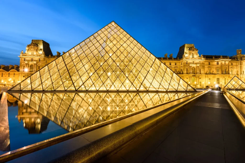 Iconic glass pyramid at the Louvre Museum in Paris under a clear sky.