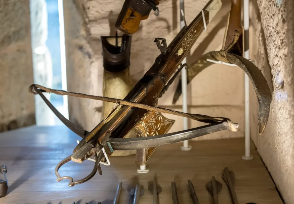 Antique medieval crossbow and arrows displayed inside a castle museum.