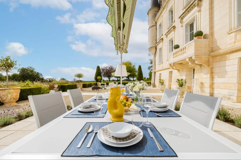 Elegant outdoor dining table set with plates, glassware, and décor in front of a château lawn