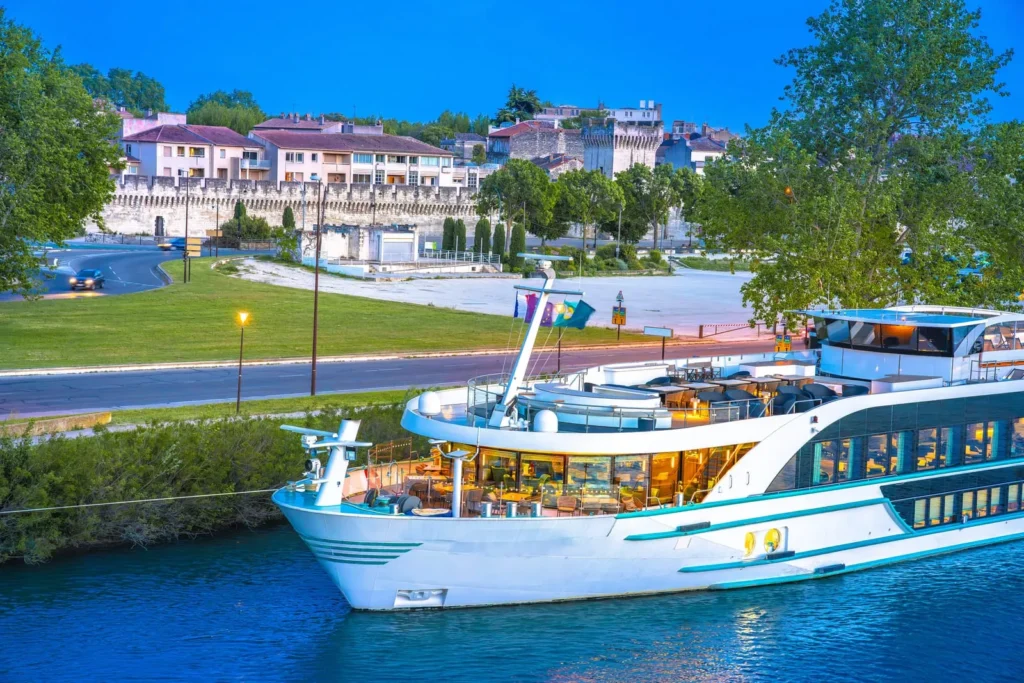 Luxury river cruise ship sailing past a historic walled town along a scenic waterfront at dusk