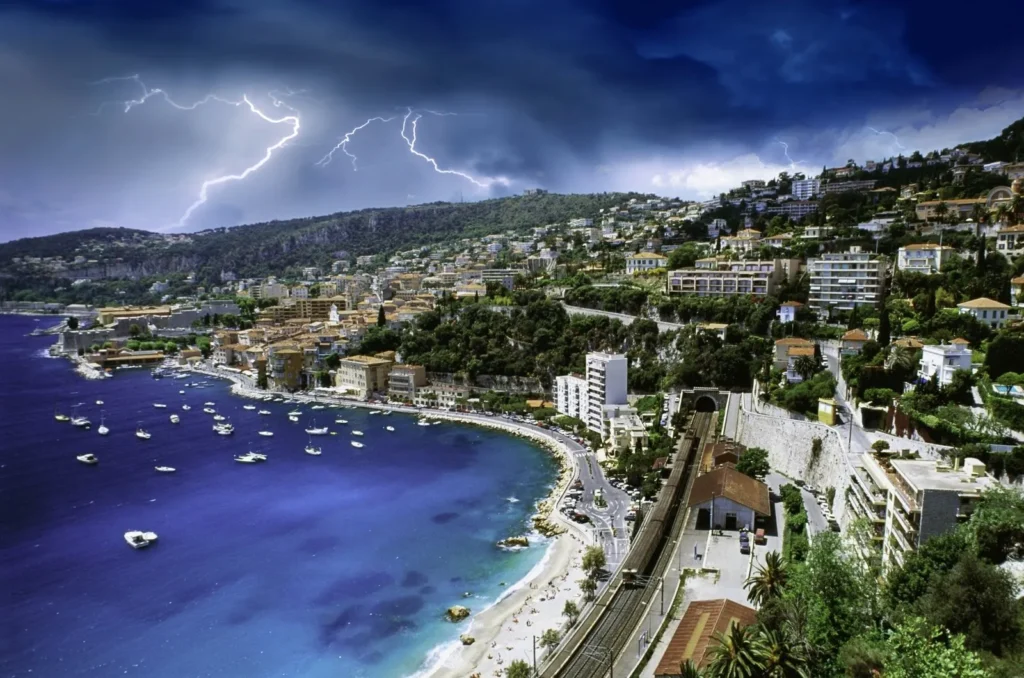 Dramatic storm clouds and lightning above the French Riviera coastline with luxury waterfront homes and boats in the bay