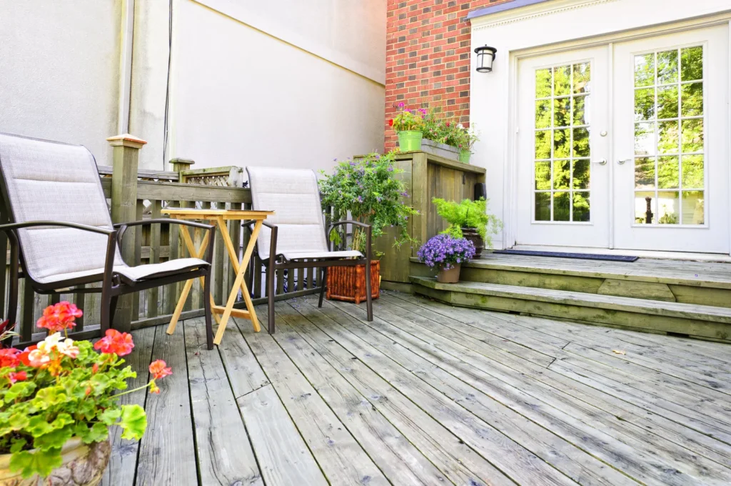 Small wooden patio deck with chairs, flowers, potted plants, and white French doors