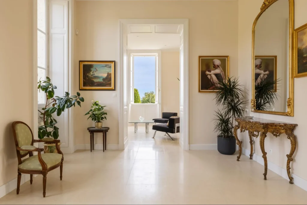 Bright French chateau hallway with antique chair, gold mirror, framed art, and soft neutral walls