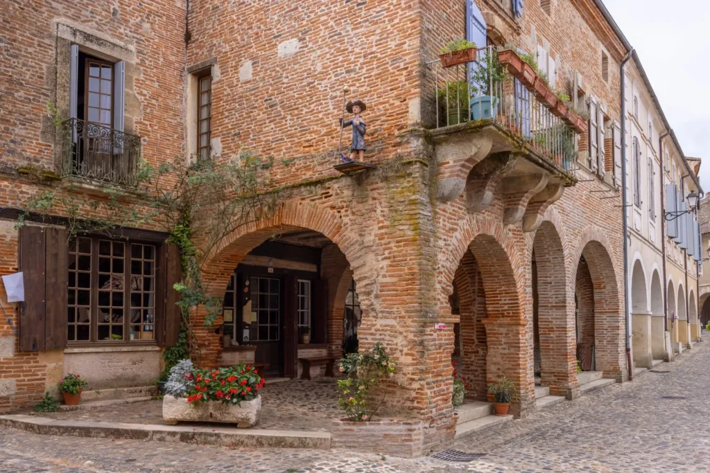 Old French brick building with arched walkways, balconies, shutters, and cobblestone street