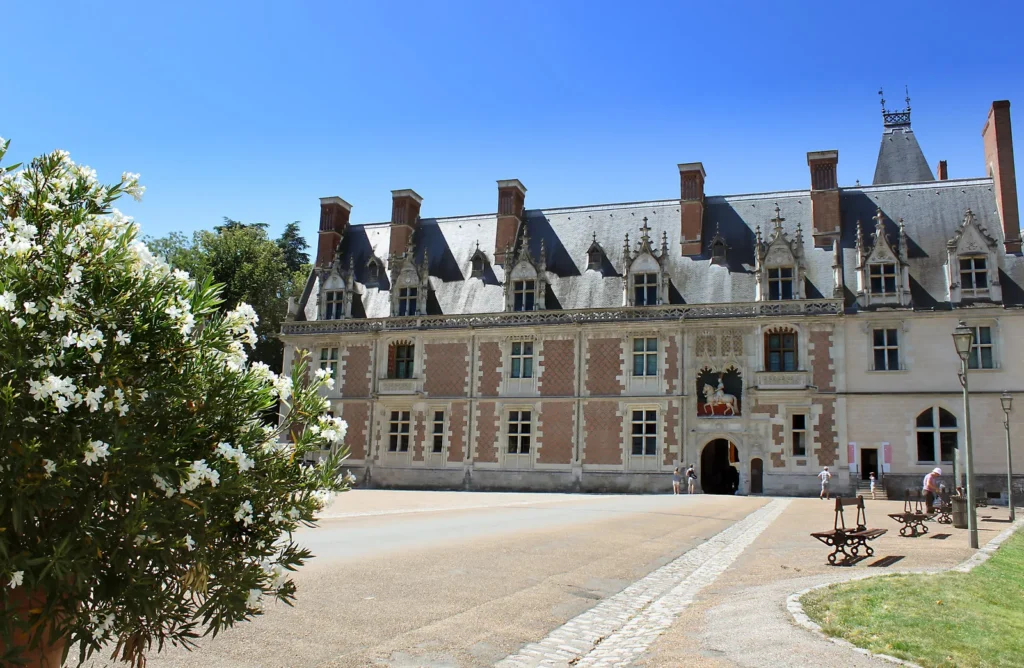 Renaissance-style French chateau with ornate windows, slate roof, and sunny courtyard.