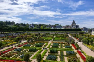 Colorful formal garden with geometric hedges, flower beds, pathways, and village church nearby