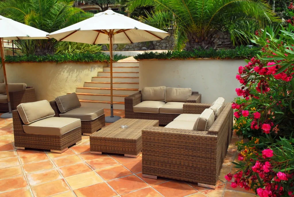 Outdoor villa patio with wicker lounge seating, umbrellas, tropical plants, and pink flowers