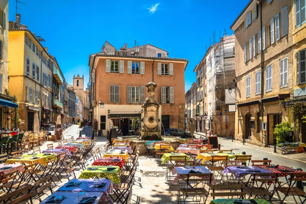 Sunny Provence town square with colorful cafe tables, historic buildings, and central fountain