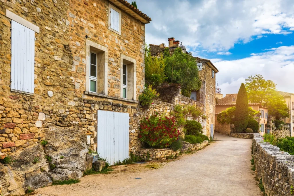 Rustic Provence village lane with stone houses, white shutters, plants, and warm sunlight