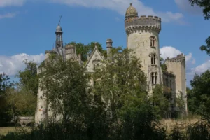Overgrown abandoned chateau with tall tower and damaged roof